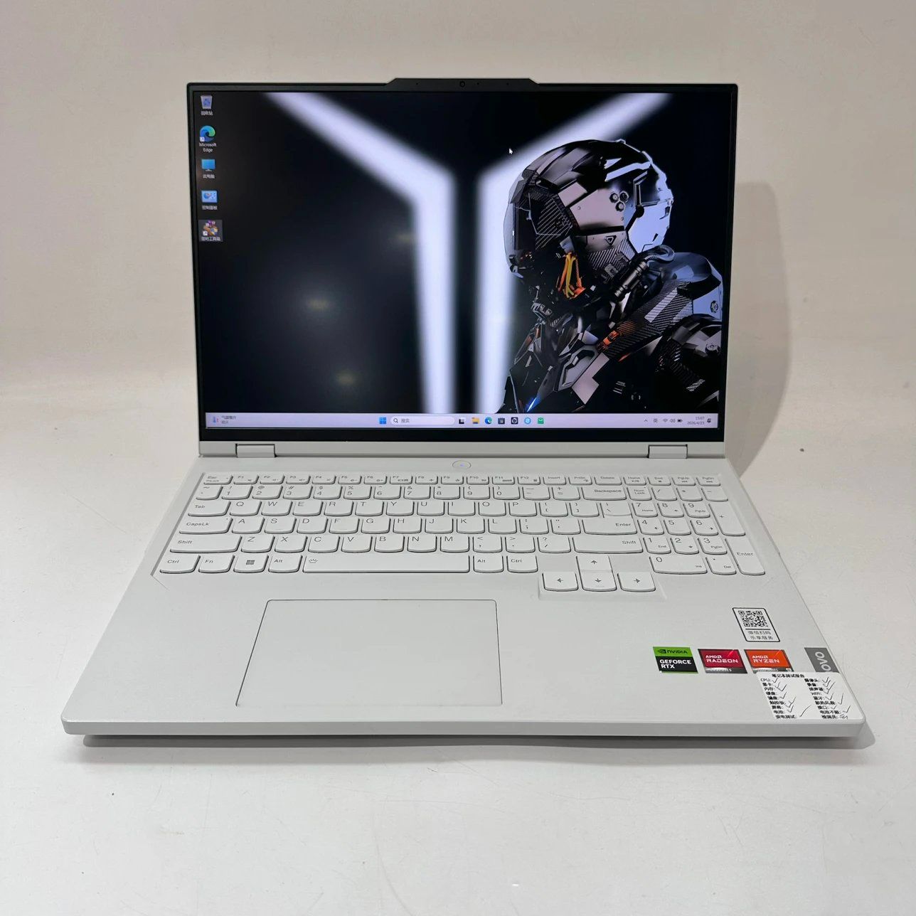 White Lenovo Legion gaming laptop open on a white surface, displaying a futuristic sci-fi soldier wallpaper, featuring a full white keyboard and AMD Ryzen, AMD Radeon, and NVIDIA GeForce RTX stickers on the palm rest.